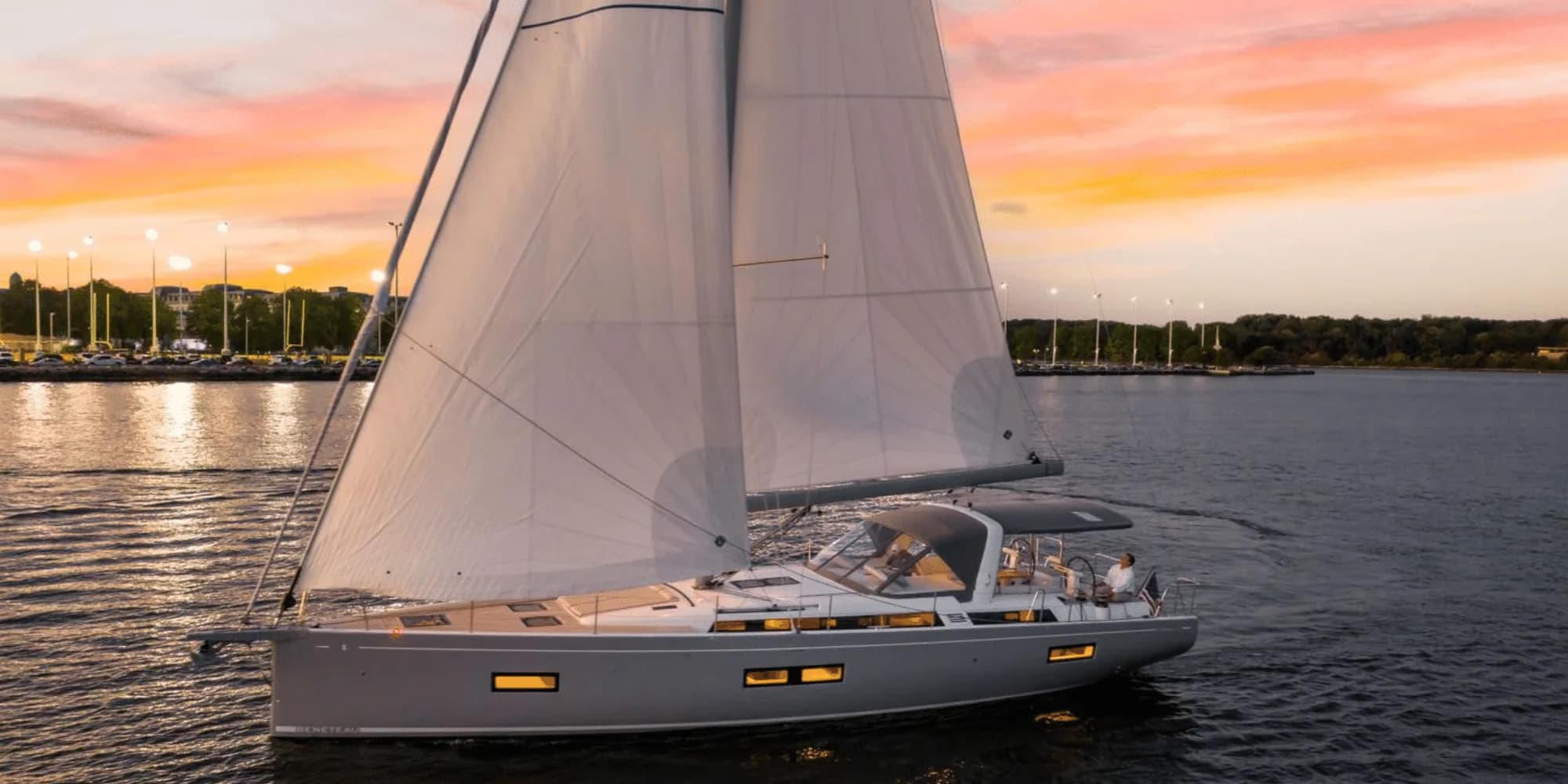 A Beneteau Oceanis Yacht 54 under sail at dusk off a lit shoreline